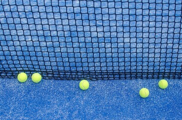 balls near the net in a blue paddle tennis court