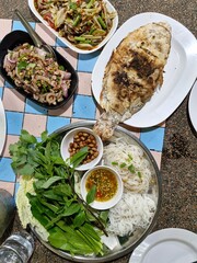 Thai food on the table, Northeastern Thai Dishes consist of Salt-grilled Fish with Fresh Herbs with Tamarind Sauce, Papaya salad with vermicelli, salted crab and fermented fish and Spicy minced pork.