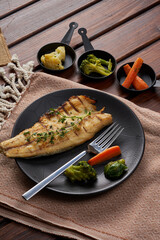 A plate of mackerel with boiled vegetables on a wooden floor