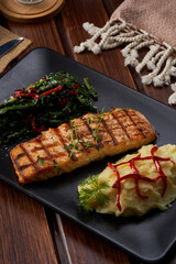 A macro shoot of a  plate of salmon with boiled vegetables on a wooden floor
