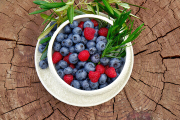 Blueberry and raspberry berries in a white plate on a wooden background. Flat lay. Copy Space.