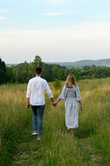 A boy and a girl are holding hands and walking in an open field
