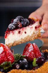 hand holding a slice of sweet pie with cream topping and berries