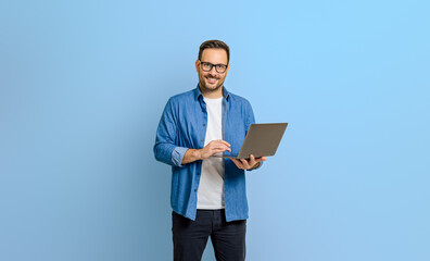Portrait of confident businessman doing online research over laptop against blue background