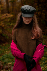 Beautiful young relaxed smiling woman in black cap and taking off her burgundy jacket and enjoying nature lake on an autumn day 