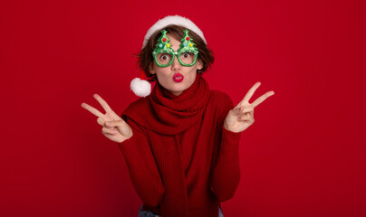 Fototapeta na wymiar Excited beautiful smiling young woman in Santa hat and Christmas glasses is posing and having fun on party on red background. Merry christmas. Happy new year. Holidays and celebration in winter