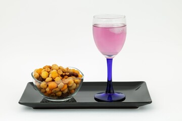 Glass of cold pink beverage with dried fruit appetizer on a plate