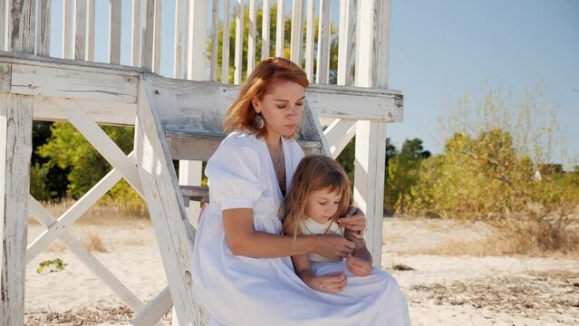 Mom and daughter in white dresses spend time together on the beach and have fun