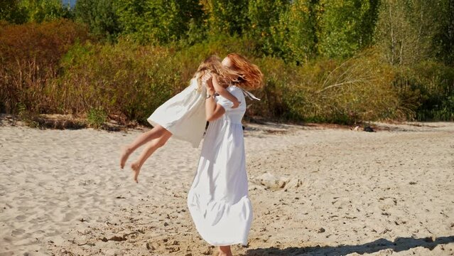 Mom spinning with her daughter and laughing on the sandy beach