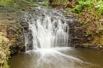 Fototapeta premium A small waterfall in the middle of the forest between dolomite rocks, long exposure