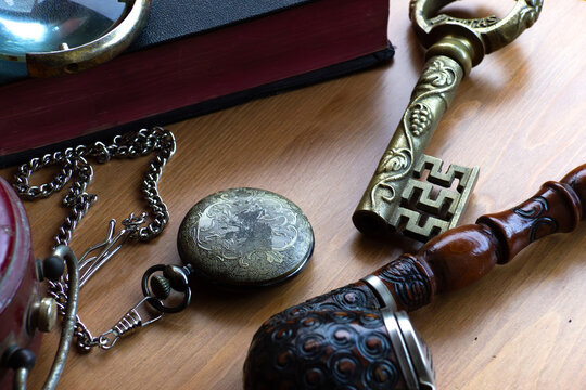 Vintage still life. Old pocket watch, antique key, smoking pipe and book with magnifier on wooden background.