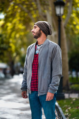 Chic guy in red-checks, beanie, strikes a stylish pose amid Madrid's green-bokeh backdrop.