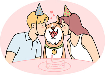 Girl, guy sit at festive table with cake, kiss dog.