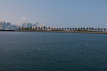 A view of the garden of the Museum of Islamic Art in Qatar, with the sea, boats and palm trees, with the Doha Towers as a background