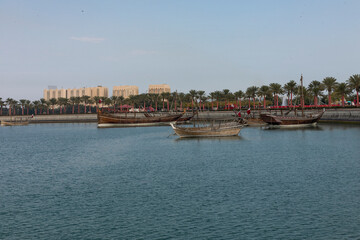 Fototapeta premium A view of the garden of the Museum of Islamic Art in Qatar, with the sea, boats and palm trees, with the Doha Towers as a background