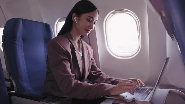 An Asian businesswoman is working on her laptop, actively recording and analyzing tasks during her flight. She is dedicated to maximizing productivity while in transit