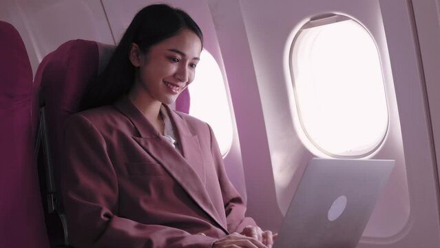 An Asian businesswoman is working on her laptop, actively recording and analyzing tasks during her flight. She is dedicated to maximizing productivity while in transit