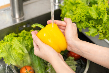 Close up hand of asian young housekeeper woman, washing sweet pepper, yellow paprika, vegetables...