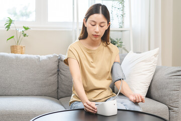 Hypotension problem asian young woman sitting on couch checking blood high pressure and heart rate...