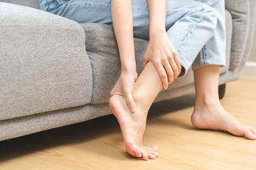 Fotobehang Foot pain concept, close up hand of young woman rubbing, massaging sore feet area of pain, girl suffering on sofa, couch at home. Discomfort painful feet ache from walking for long. Physical injury. © KMPZZZ
