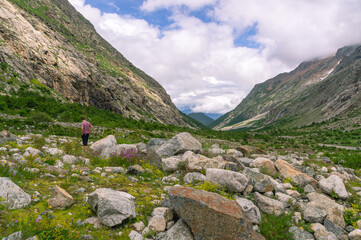 Panorama in the mountains. Granite stones and flowers in the highlands. A trip to the mountains. View of the mountains, clouds and flowers. Hiking in summer. A man walks on rocks in the mountains.