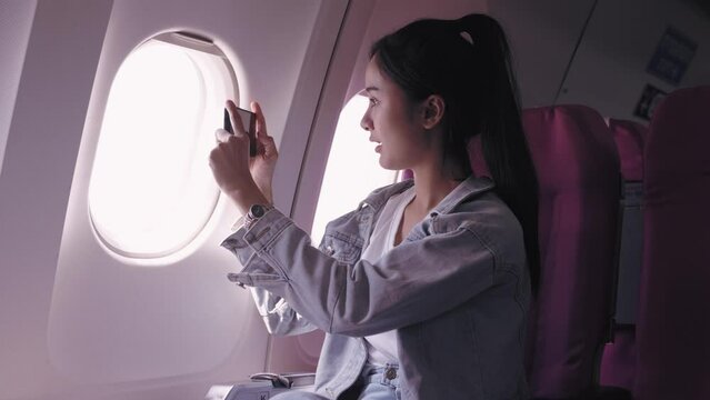 Asian female tourists, currently on an airplane journey, are excitedly capturing pictures of the sky from the plane window, immersed in the beauty of the moment. capture the joy and beauty of travel.