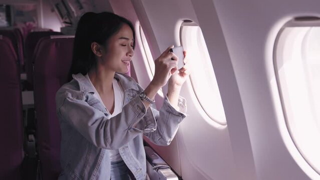 Asian female tourists, currently on an airplane journey, are excitedly capturing pictures of the sky from the plane window, immersed in the beauty of the moment. capture the joy and beauty of travel.