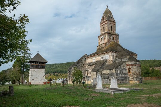 Rural church with a graveyard in the background set against a dark, cloudy sky: The Densus Church