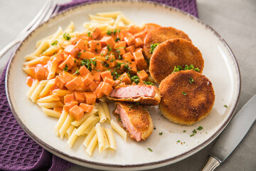 Jägerschnitzel nach DDR GDR Rezept mit Jagdwurst paniert, Makkaroni Penne Nudeln, Tomatensoße, Petersilie mit Teller, Besteck, lila Serviette und Marmor Hintergrund