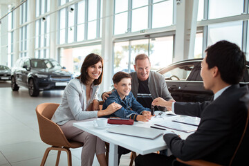 Family with young boy taking car key from auto salesman