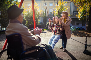 Granddaughter and grandmother have fun with swing while grandfather watches in the park