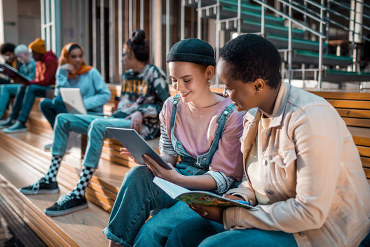Two Students Sharing a Tablet for Studying on Campus Steps