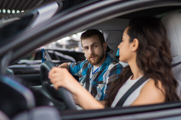 Female learner driver student sitting in the car. Male instructor holding paper while looking at her. Test drive, transportation, safety, education concept