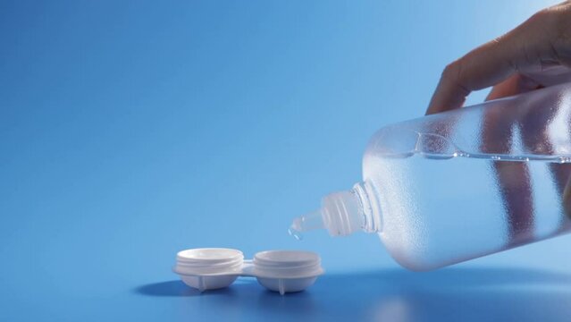 lens solution, female hands pouring cleaning liquid from a bottle into a contact lens case on a blue background