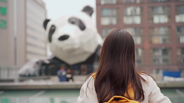 Young woman traveler takes a photo of a giant panda statue while traveling in Chengdu, China