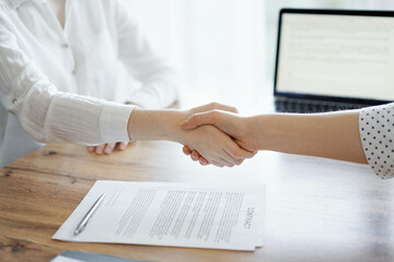 Business people shaking hands above contract papers just signed on the wooden table, close up. Lawyers at meeting. Teamwork, partnership, success concept