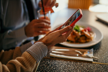 Female taking a photo with a smartphone of a food before eating in the bright venue.