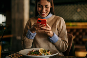 Smiling woman photographing a food before eating in the restaurant.