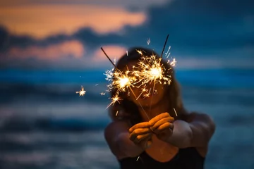 Foto op Plexiglas Young woman holding sparkler celebrating new years eve on the beach © fotomaximum