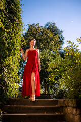 glamouröse Frau in einem roten Kleid auf einer Steintreppe im Park