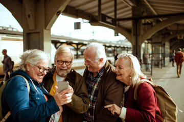 Senior people friends looking at mobile phone in train station