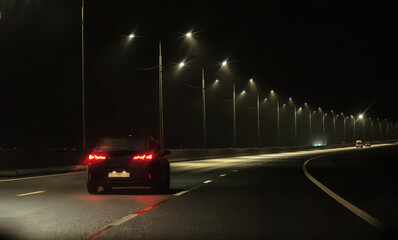 A passenger car is driving on a night highway. A car on a foggy highway. Bad weather for motorists.