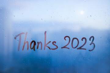 lettering Thanks and numbers 2023 paint with finger with streaks of water on splashed by rain foggy glass on blue window