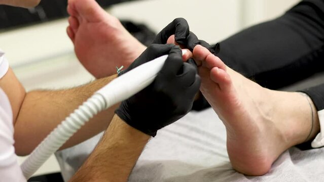 A close-up of an unrecognizable professional podiatrist is performing a pedicure treatment on a patient. The worker files the calluses of a patient for healthy foot hygiene.