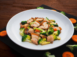 Stir fried mixed vegetables with crispy pork in plate on wooden table background. Thai Food