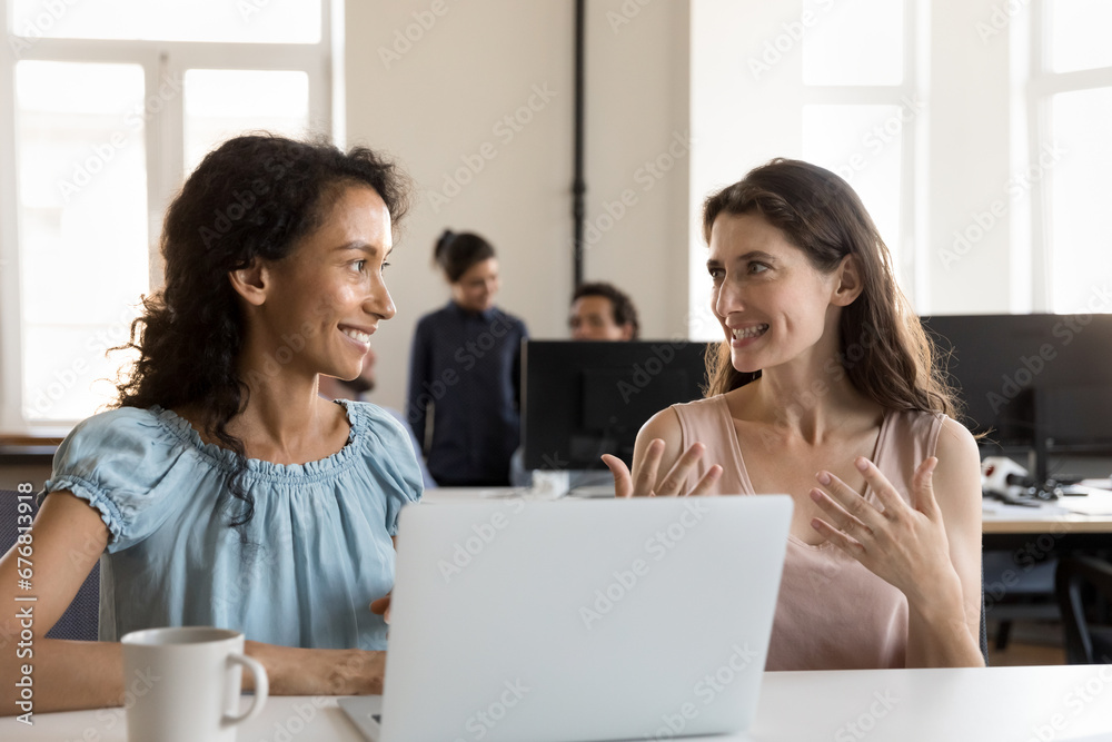 Sticker two happy multiethnic employees cooperating on project at shared laptop, workplace, talking, discuss