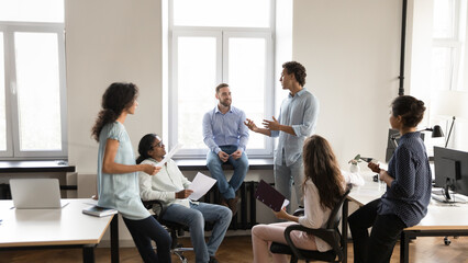 Diverse young business team employee speaking to group of colleagues, sharing ideas on office meeting, talking to group. Corporate teacher, mentor training multiethnic staff. Banner shot