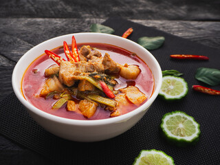 Red curry with pork belly and water spinach in bowl on wooden table background. ( GANG TAY PO ) Thai Food
