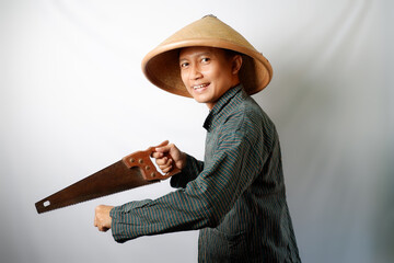 Happy Asian farmer wearing Lurik and Caping cutting something using a saw isolated on white background.