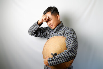 Indonesian farmer wearing Lurik holding a Caping standing with sad expression isolated on white background.